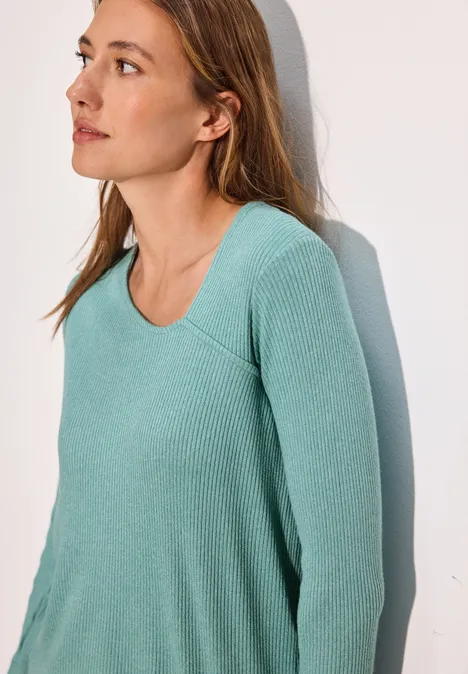 Frau mit langen Haaren trägt einen türkisfarbenen, gerippten Pullover.